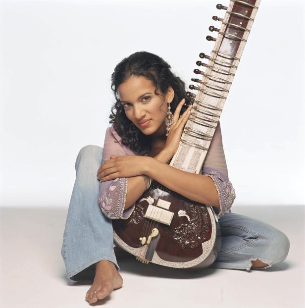 Eine Frau sitzt barfuß da und hält eine Sitar in ihren Armen.