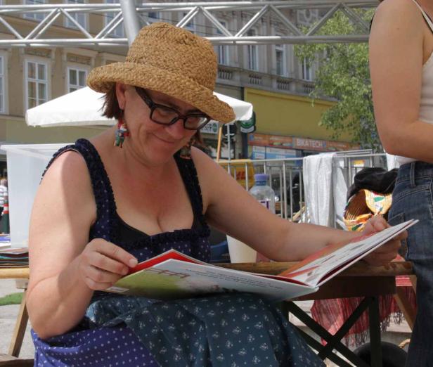 Eine Frau mit Hut und Brille liest ein Buch im Freien.