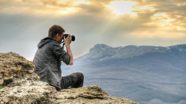 Ein Fotograf sitzt auf einem Felsen und fotografiert die Landschaft.