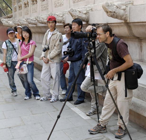 Eine Gruppe von Touristen und ein Fotograf mit Stativ vor einer verzierten Mauer.