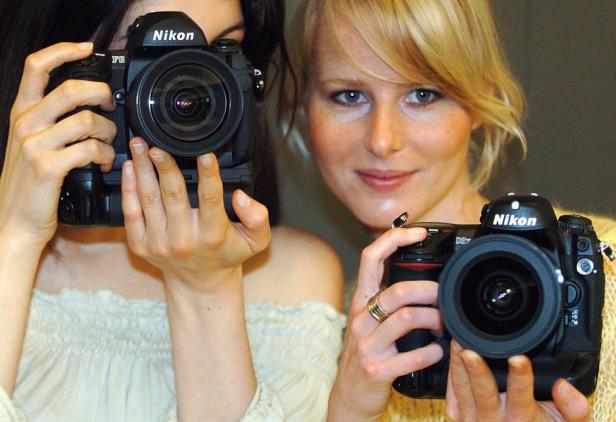 Zwei Frauen halten Nikon-Kameras vor ihre Gesichter.