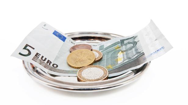 Ein silbernes Tablett enthält einen Fünf-Euro-Schein und ein paar Münzen.