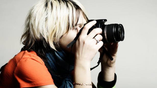 Eine Frau mit blond gesträhnten Haaren fotografiert mit einer Spiegelreflexkamera.