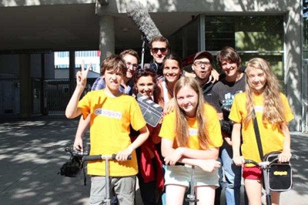 Eine Gruppe von Kindern und Erwachsenen posiert mit einer Filmklappe und Rollern für ein Foto.