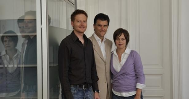 Drei Personen posieren vor einer weißen Wand für ein Foto.