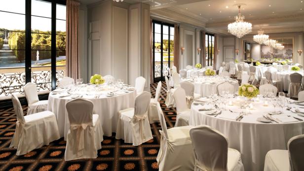 Ein elegant dekorierter Ballsaal mit runden Tischen und Blick auf einen formellen Garten.