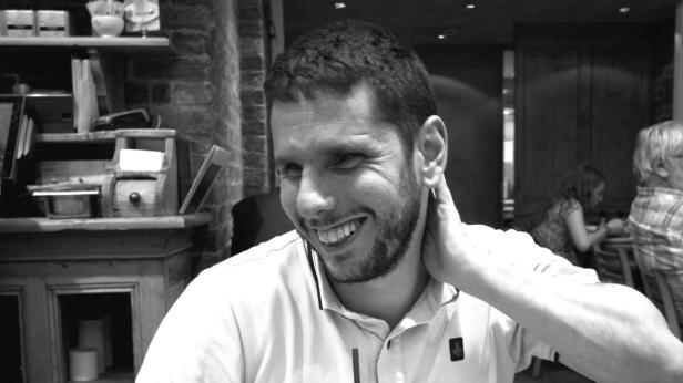 Ein lächelnder Mann sitzt in einem Restaurant und hält sich an den Nacken.