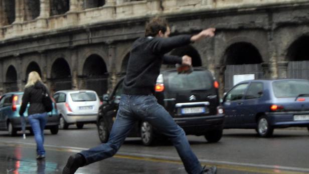 Ein Mann rennt mit erhobenem Arm über eine Straße in Rom, im Hintergrund das Kolosseum.