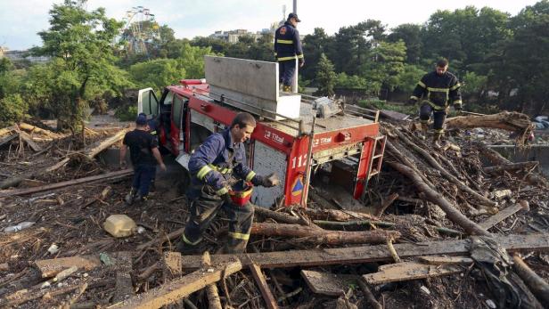 Feuerwehrleute arbeiten inmitten von Trümmern und einem beschädigten Feuerwehrwagen nach einer Überschwemmung.