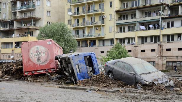 Ein Coca-Cola-LKW, ein umgekippter Lastwagen und ein Auto sind von einer Schlammlawine beschädigt.
