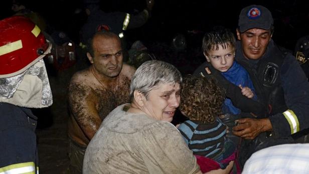 Eine weinende Frau und ein schlammbedeckter Mann werden von Rettungskräften und ihren Kindern umgeben.