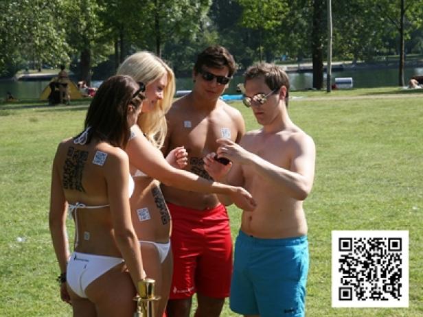 Eine Gruppe junger Leute steht im Freien, einige mit aufgeklebten QR-Codes auf dem Körper.