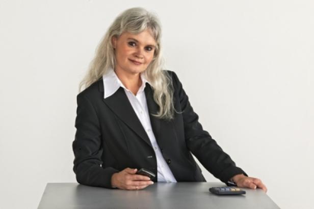 Eine Frau im Blazer steht an einem Tisch mit einem Taschenrechner und einem Mobiltelefon.