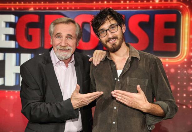 Zwei Männer posieren vor dem roten Hintergrund einer Fernsehshow.