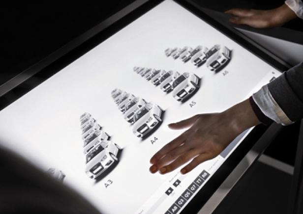 Eine Person interagiert mit einem interaktiven Display, das verschiedene Audi-Modelle zeigt.