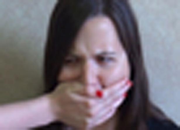 Eine Frau mit dunklen Haaren, deren Mund mit einer Hand zugehalten wird.