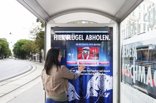 Red Bull - Special Edition - Ambient Media-Kampagne - Sampling-Promotion - Gewista City Light Eine Frau interagiert mit einem Red Bull Fotoautomaten an einer Bushaltestelle.