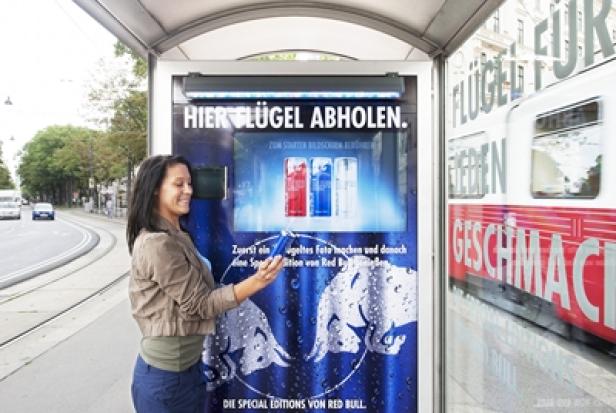 Red Bull - Special Edition - Ambient Media-Kampagne - Sampling-Promotion - Gewista City Light Eine Frau fotografiert eine Red Bull-Werbung an einer Bushaltestelle.