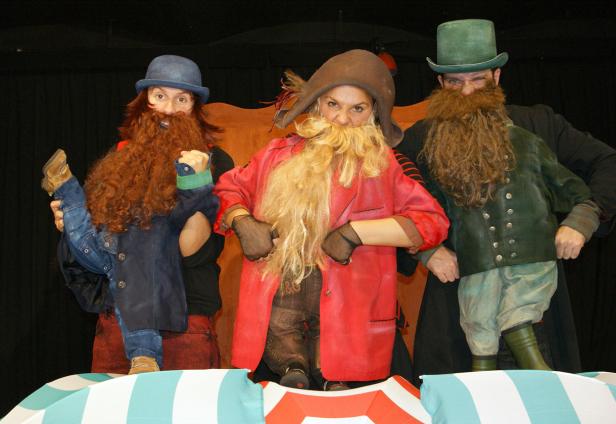 Drei Personen in Kostümen und falschen Bärten stehen auf einer Bühne.