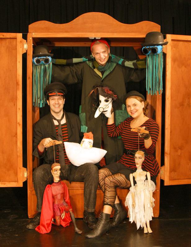 Drei Puppenspieler mit ihren Puppen in einem hölzernen Schrank.