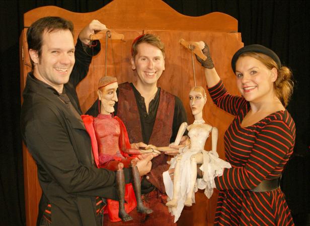 Drei Personen präsentieren ein Marionettentheater mit zwei Marionetten.