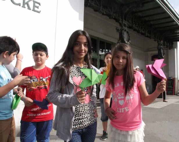 Eine Gruppe von Kindern hält bunte Origami-Figuren in der Hand.