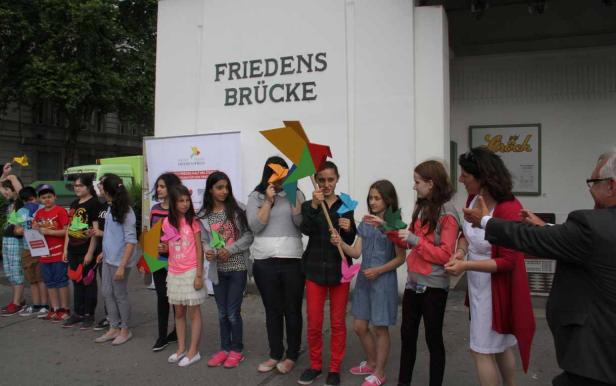 Eine Gruppe von Kindern und Erwachsenen steht vor der „Friedensbrücke“ und hält Papierkunstwerke.