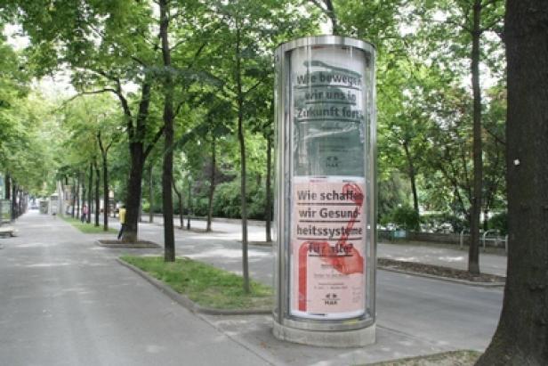 MAK Museum für angewandte Kunst Wien - Positionierungskampagne - MediaCom Vienna Eine Litfaßsäule mit Werbung steht am Straßenrand in einer von Bäumen gesäumten Allee.