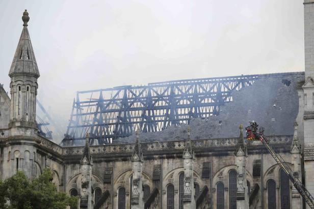 Ein Feuerwehrmann auf einer Drehleiter untersucht das beschädigte Dach einer Kirche.