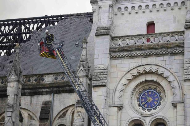 Ein Feuerwehrmann in einem Hubsteiger untersucht das beschädigte Dach einer Kirche.