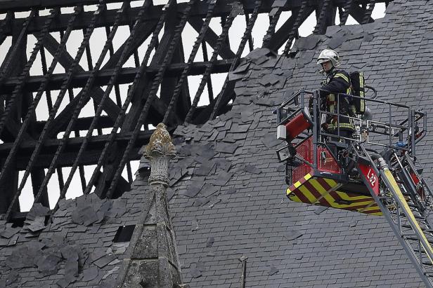 Ein Feuerwehrmann steht auf einer Drehleiter vor einem beschädigten Dach.