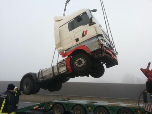 Ein beschädigter LKW wird mit einem Kran auf einen Tieflader gehoben.