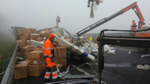 Ein umgestürzter Lastwagen liegt auf der Seite, während Arbeiter mit einem Kran die Ladung bergen.
