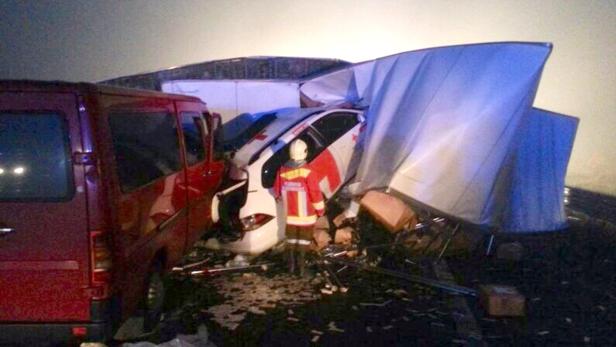 Ein Feuerwehrmann steht an der Unfallstelle, wo ein roter Lieferwagen und ein Lastwagen beteiligt sind.