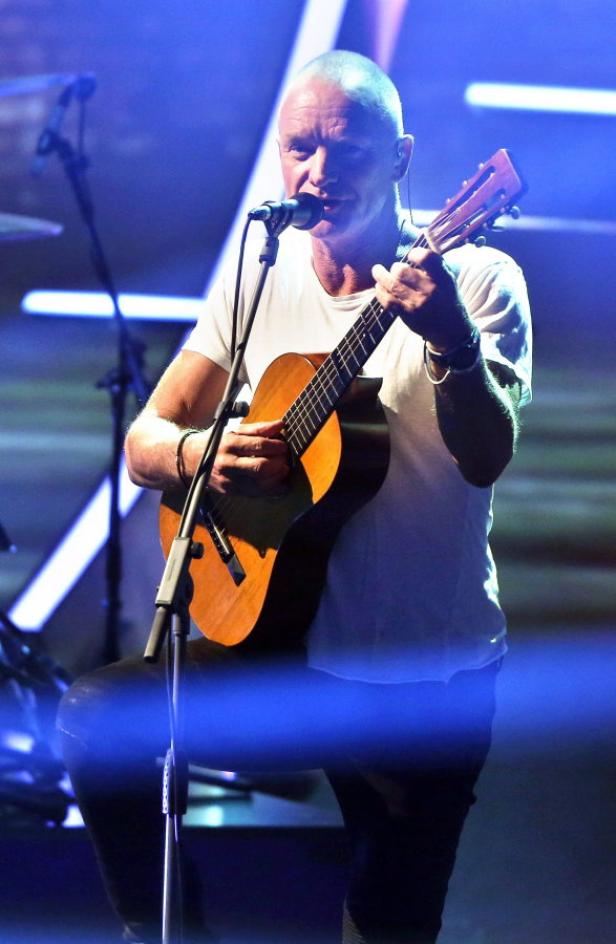 Sting tritt mit einer Akustikgitarre auf einer Bühne auf.
