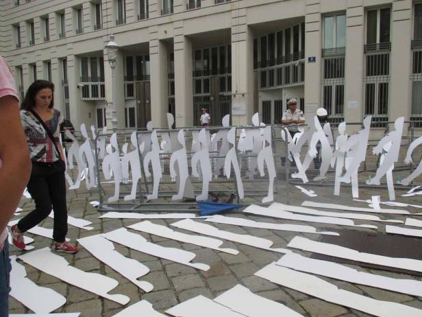 Eine Frau geht an einer Installation aus weißen Pappfiguren vorbei.