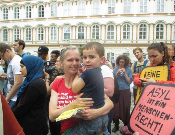 Eine Frau hält ein Kind auf einer Demonstration mit Schildern, die „Asyl ist ein Menschenrecht“ fordern.