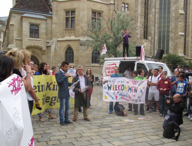 Eine Gruppe von Menschen demonstriert mit Schildern und einem Transparent, auf dem „Willkommen“ steht.