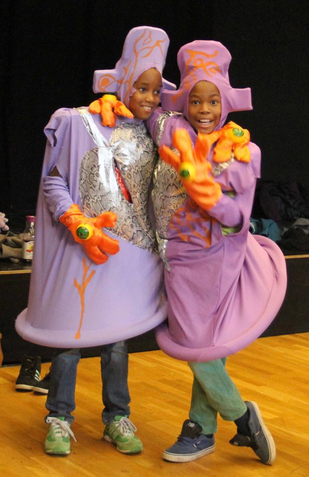 Zwei Kinder posieren in lila Kostümen mit orangefarbenen Akzenten.