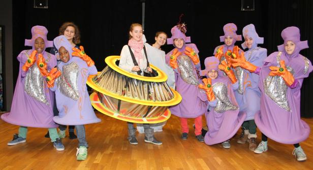 Eine Gruppe von Kindern in fantasievollen, lilafarbenen Kostümen steht auf einer Bühne.