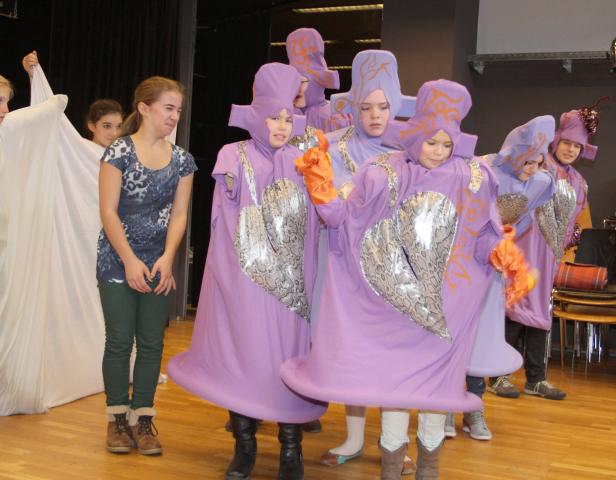Eine Gruppe von Kindern in lila Kostümen mit seltsamen Hüten auf einer Bühne.