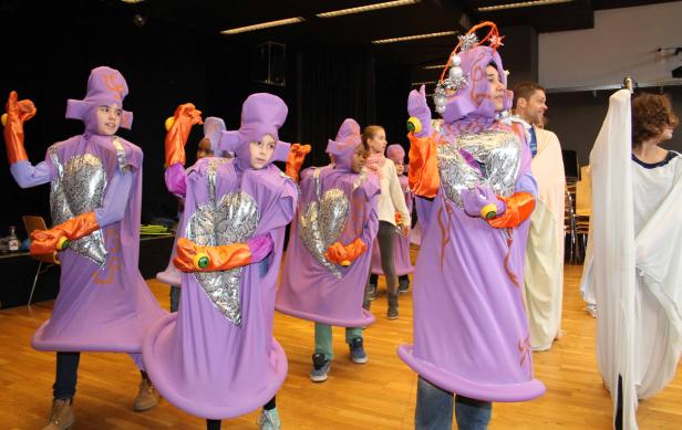 Kinder in lila Kostümen treten auf einer Bühne auf.