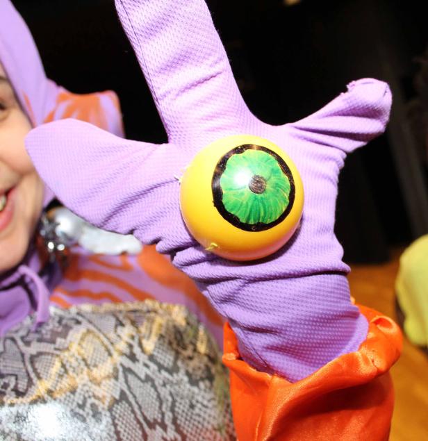 Eine Person in einem Kostüm hält einen gelben Ball mit einem grünen Auge darauf.