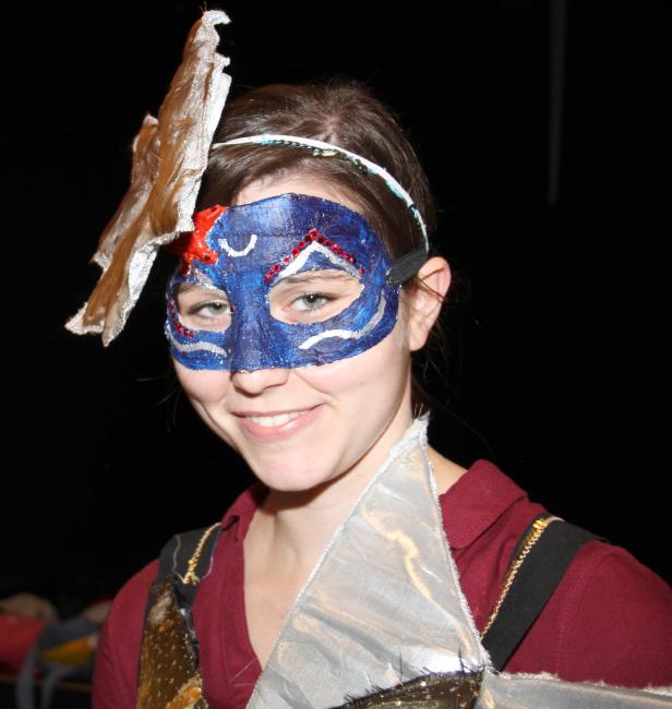 Eine lächelnde Person mit einer blauen, verzierten Maske und einem Kostüm.