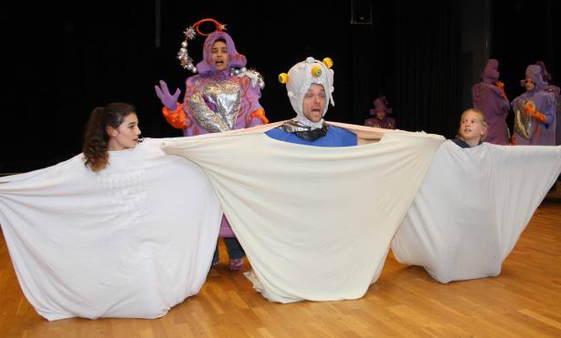 Personen in Kostümen halten ein weißes Tuch auf einer Bühne.