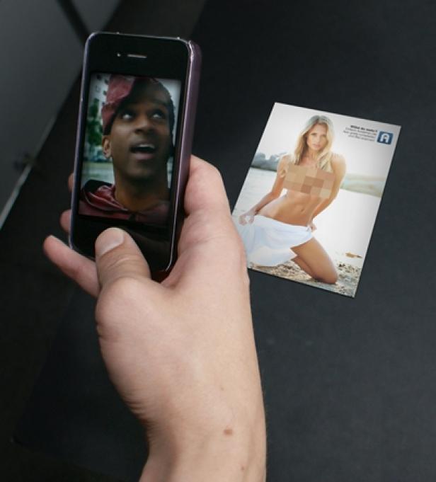 Eine Hand hält ein Smartphone mit einem Foto eines Mannes, daneben ein freizügiges Werbeplakat.
