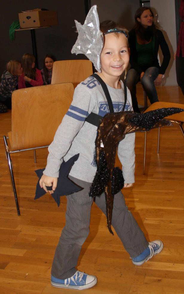 Ein lächelnder Junge in einem selbstgemachten Sternenkostüm geht über einen Holzboden.