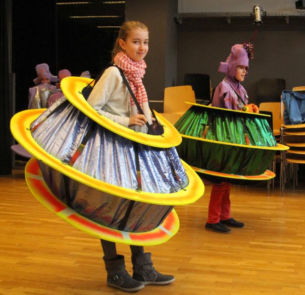 Zwei Kinder in Kostümen, die Planeten darstellen, stehen in einem Raum.