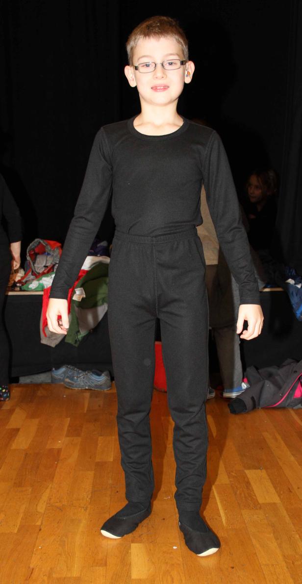 Ein Junge mit Brille trägt ein schwarzes Kostüm auf einer Bühne.