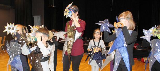 Eine Gruppe von Kindern und eine Frau in fantasievollen, sternförmigen Kostümen auf einer Bühne.